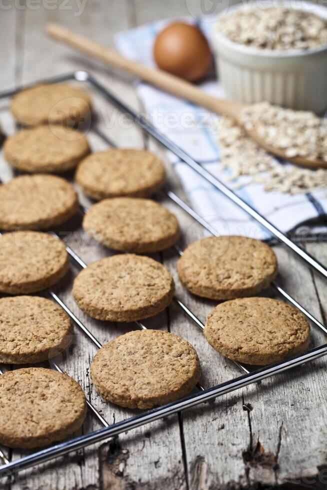 Baking grid with fresh oat cookies on rustic wooden table background, ingredients and kitchen utensil closeup on rustic wooden table. photo