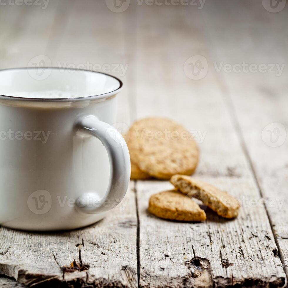 Cup of fresh milk and some homemade baked oat cookies on rustic wooden table background. photo