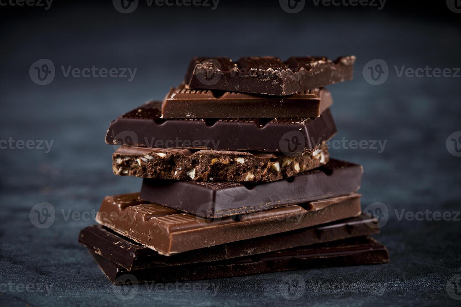 Chocolate bars pieces stack on black background. Sweet food photo concept.
