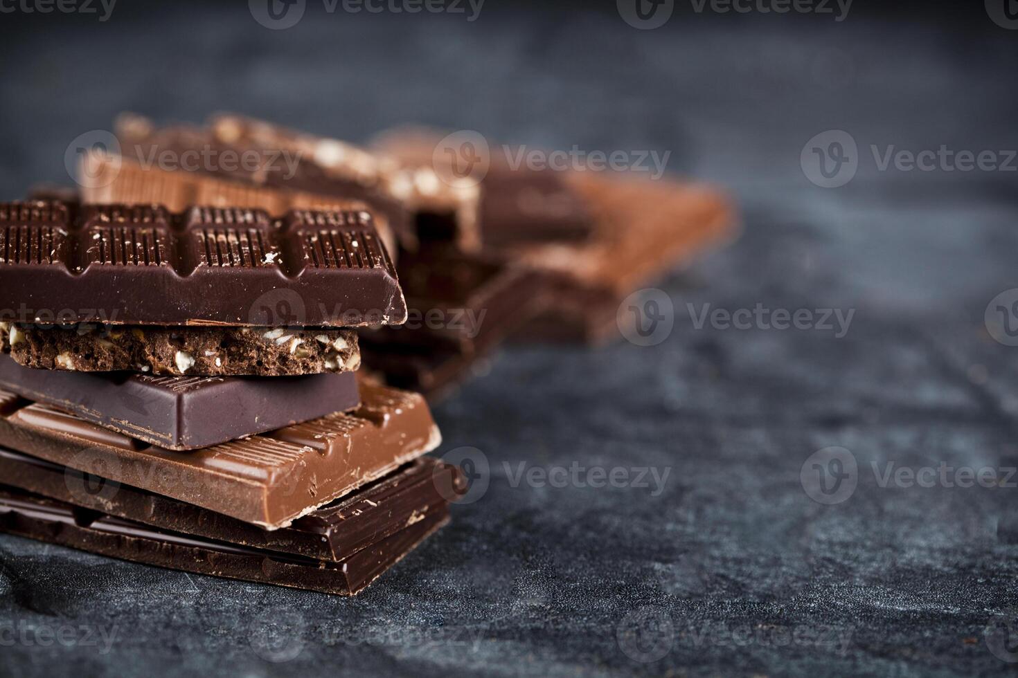 Chunks of broken chocolate stacked on black board. Chocolate bars pieces stack on black background. photo