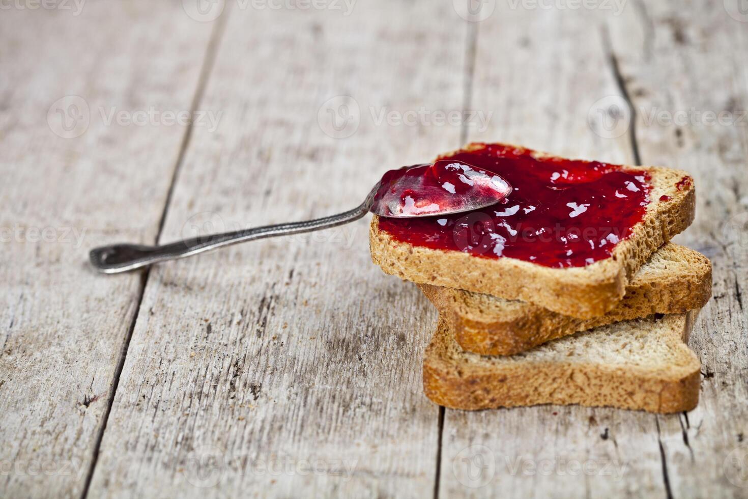 Toasted cereal bread slices with homemade cherry jam and spoon closeup on rustic wooden table background. photo