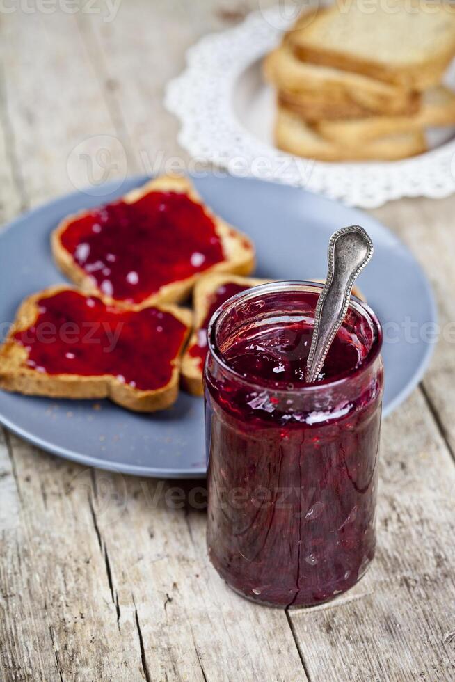 Homemade cherry jam and fresh toasted cereal bread slices plates closeup on rustic wooden table background. photo