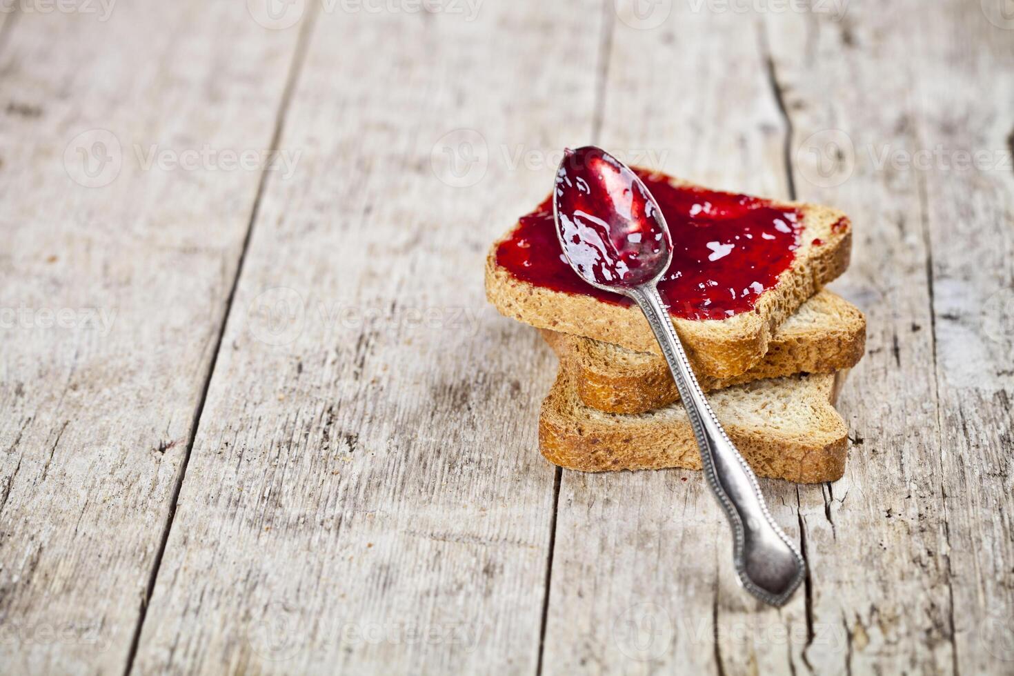 Toasted cereal bread slices stack with homemade cherry jam and spoon closeup on rustic wooden table background. photo