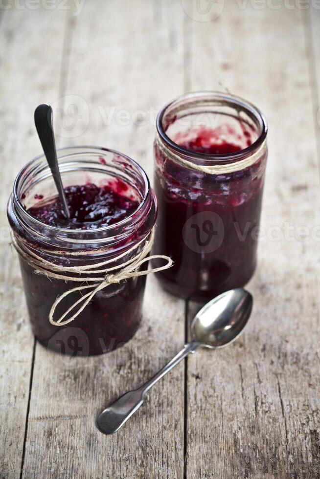 Two jars of fresh cherry and wild berries homemade jam in jar on rustic wooden background. photo