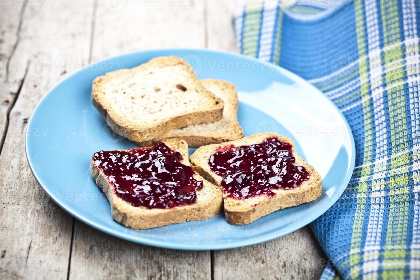 Fresh toasted cereal bread slices with homemade wild berries jam and linen napkin on blue ceramic plate closeup on rustic wooden background. photo