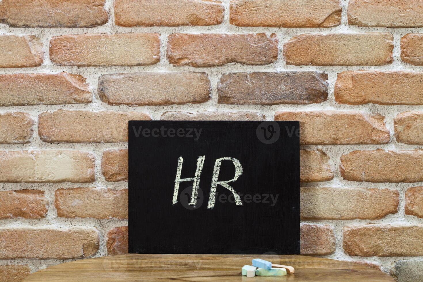 Chalk board with the word HR drown by hand and chalks on wooden table on brick wall background. photo