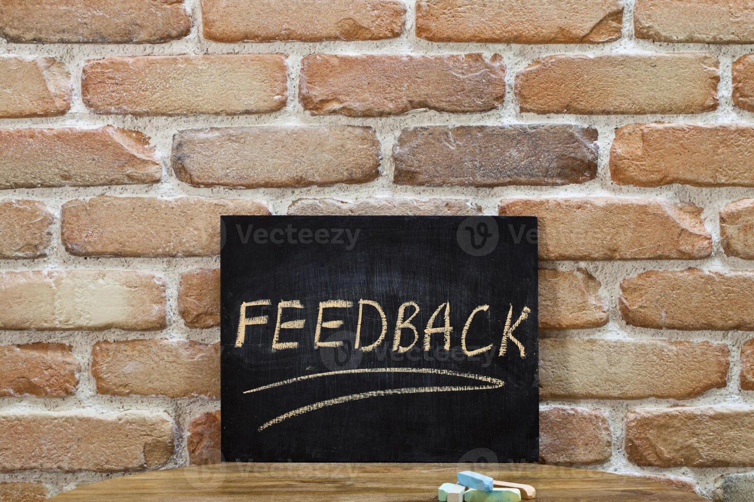 Chalk board with the word FEEDBACK drown by hand and chalks on wooden table on brick wall background. photo