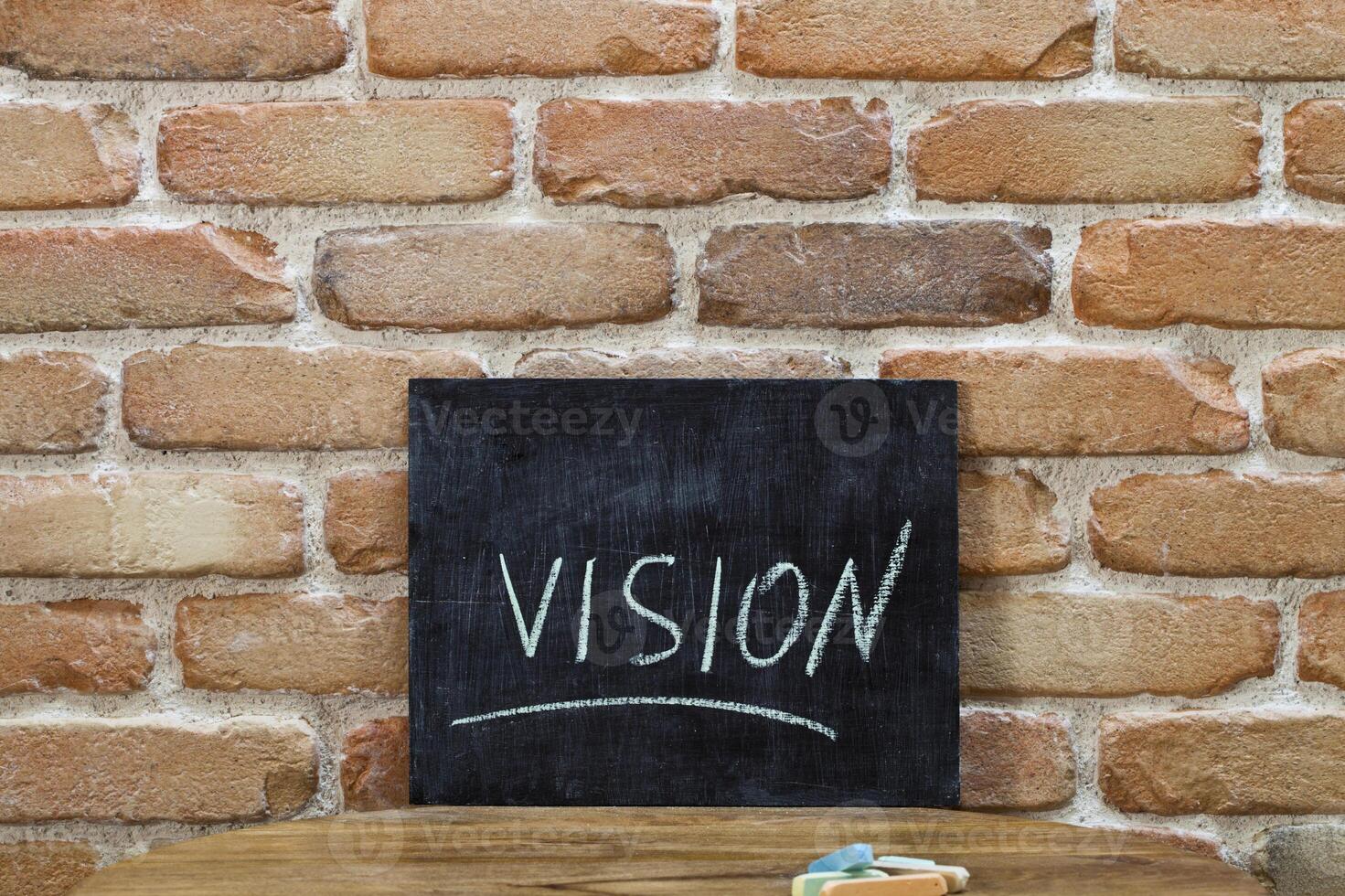 Chalk board with the word VISION drown by hand and chalks on wooden table on brick wall background. photo