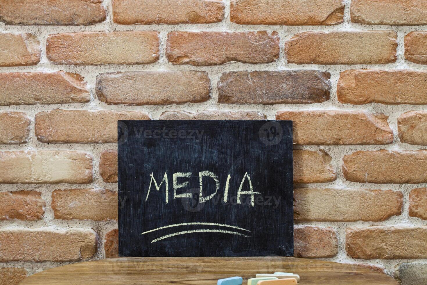 Chalk board with the word MEDIA drown by hand and chalks on wooden table on brick wall background. photo