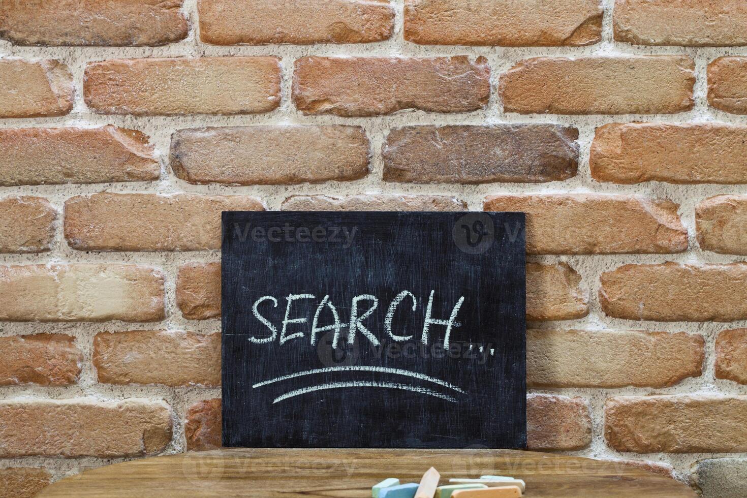 Chalk board with the word SEARCH drown by hand and chalks on wooden table on brick wall background. photo