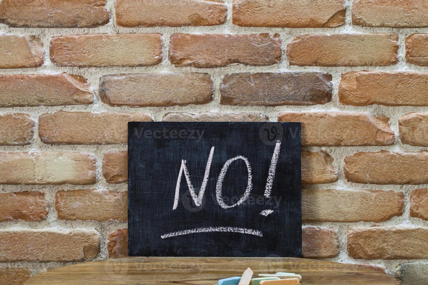 Chalk board with the word NO drown by hand and chalks on wooden table on brick wall background. photo