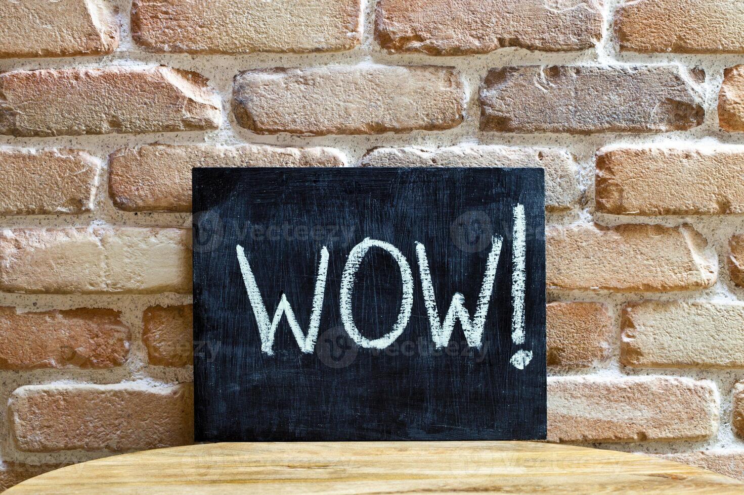 Chalk board with the word WOW drown by hand and chalks on wooden table on brick wall background. photo