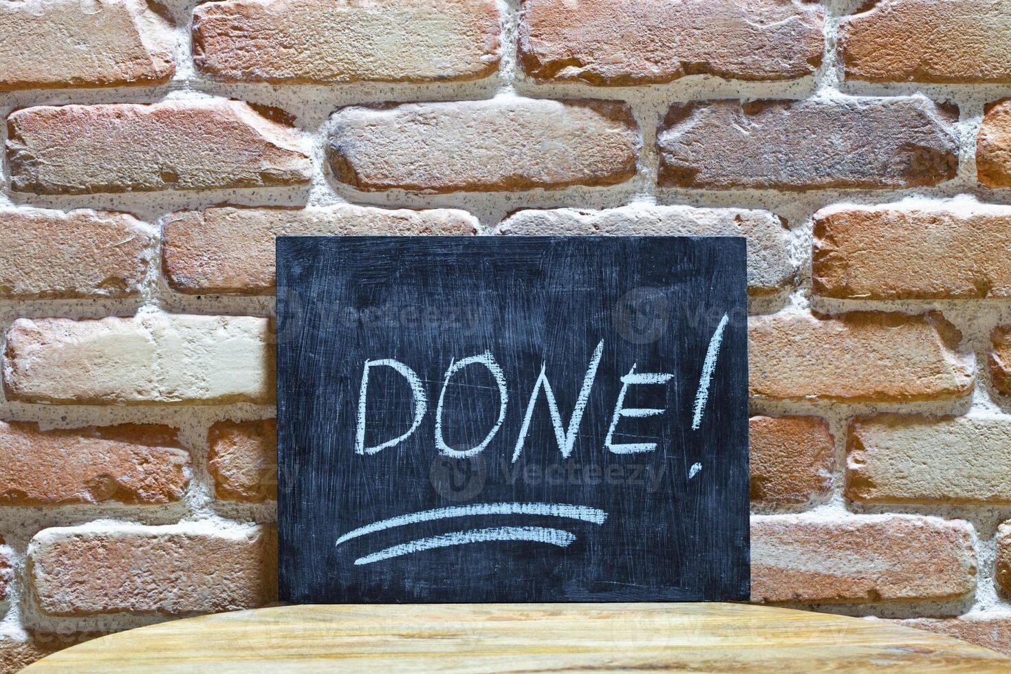Chalk board with the word DONE drown by hand and chalks on wooden table on brick wall background. photo