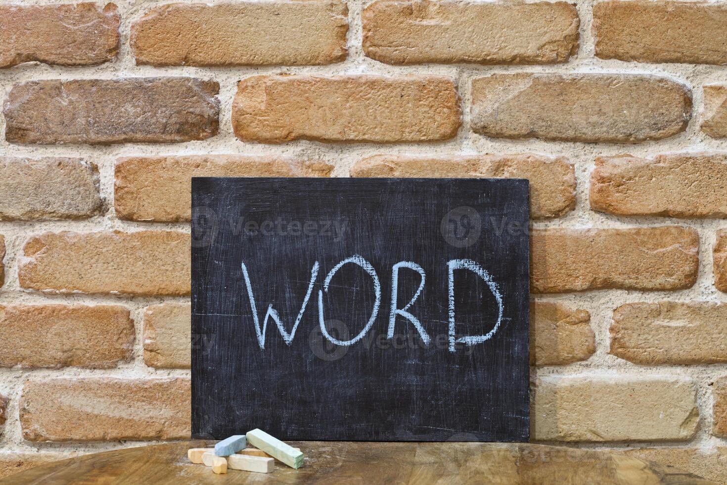 Chalk board with the word WORD drown by hand and chalks on wooden table on brick wall background. photo