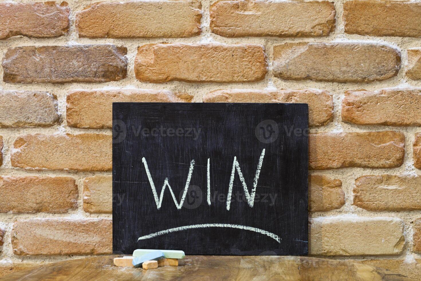 Chalk board with the word WIN drown by hand and chalks on wooden table on brick wall background. photo