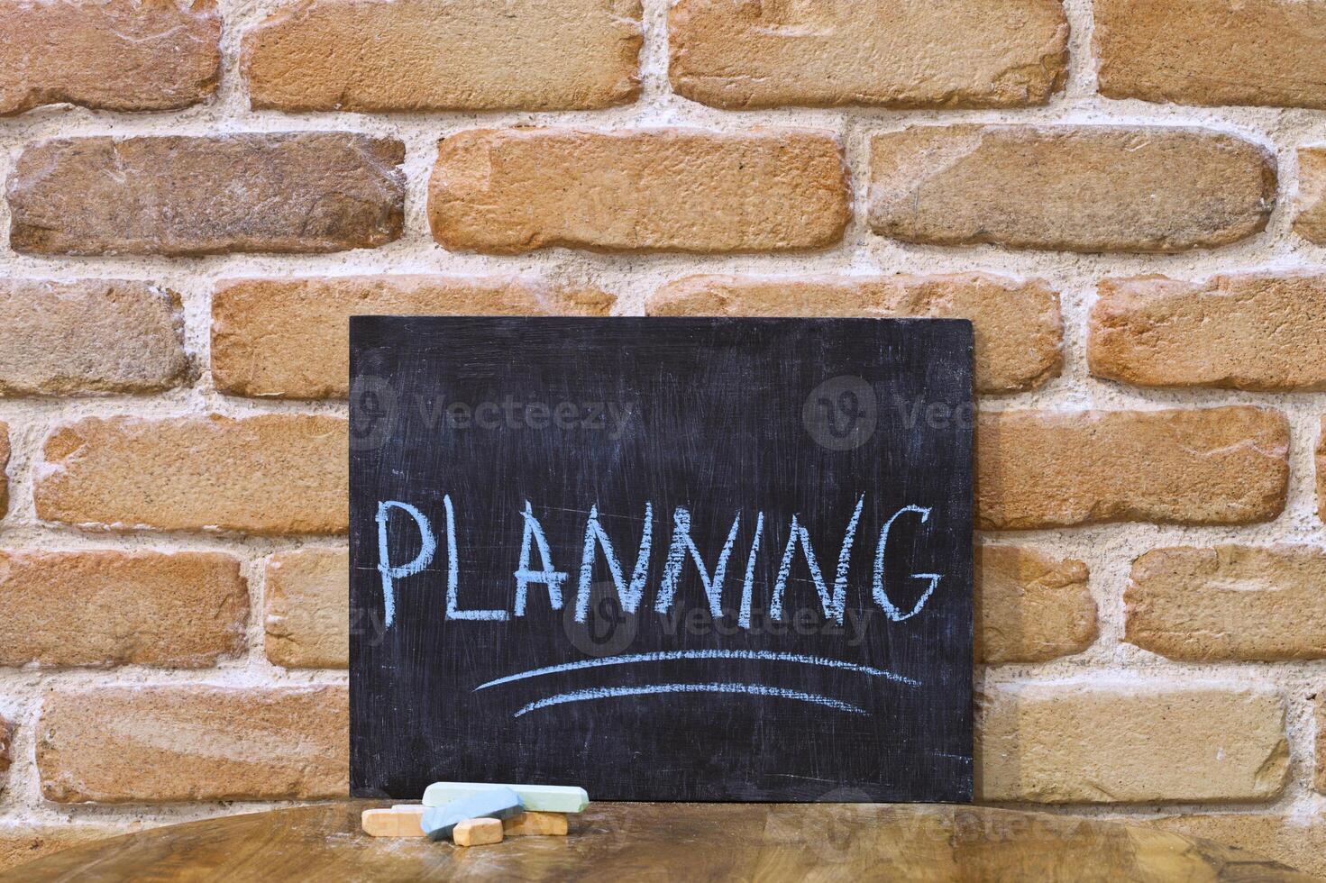 Chalk board with the word PLANNING drown by hand and chalks on wooden table on brick wall background. photo