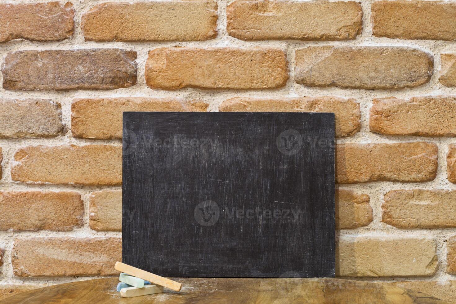 Blank clean blackboard an chalk on wooden table at brick wall. photo