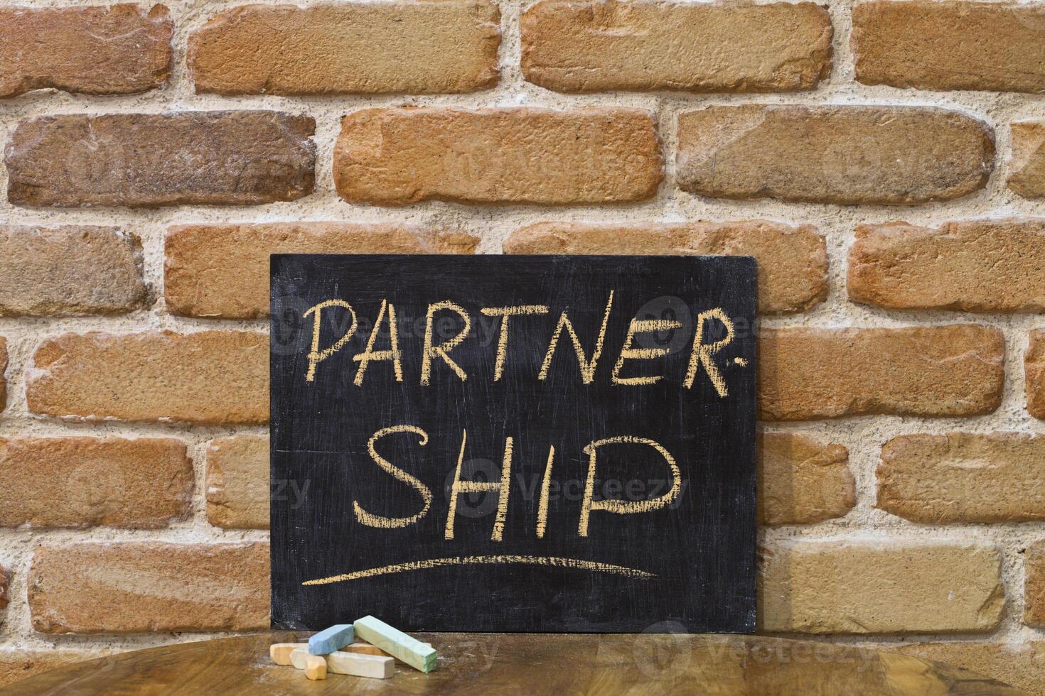 Chalk board with the word PARTNERSHIP drown by hand and chalks on wooden table on brick wall background. photo