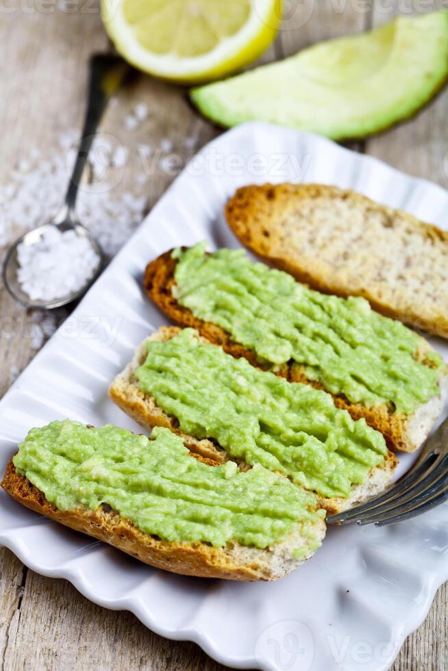 Croutons with avocado guacamole on white plate closeup on rustic wooden table. photo