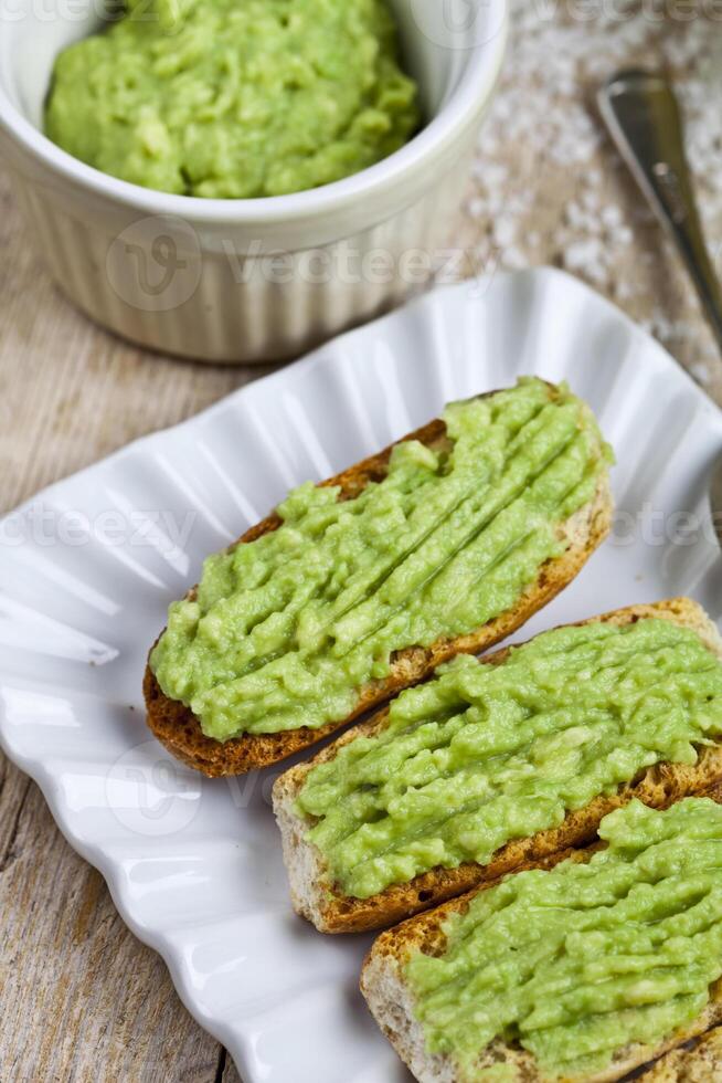 Fresh crostini with avocado guacamole on white plate closeup on rustic wooden table. photo