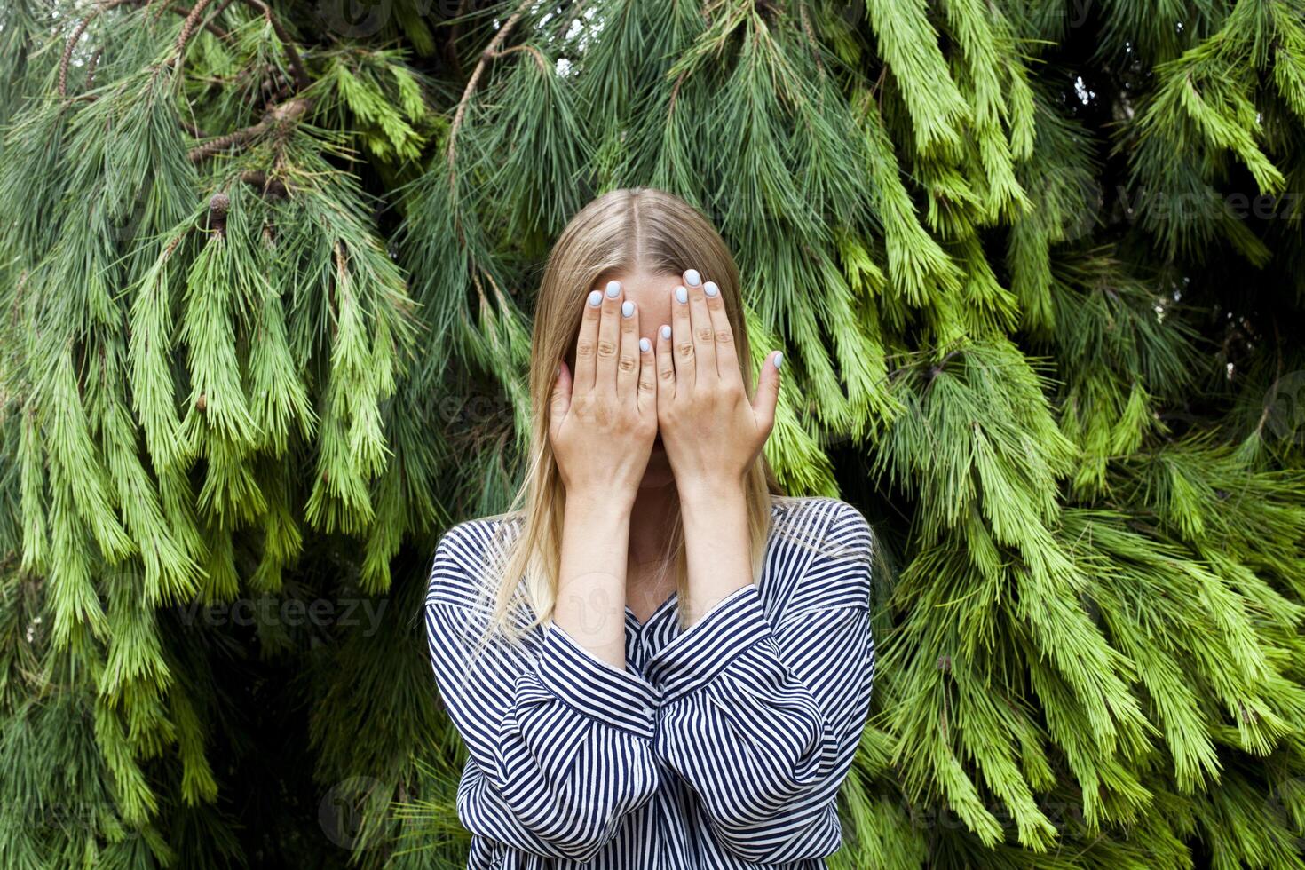 Beautiful young woman hiding her face standing in the forest against fir trees. photo
