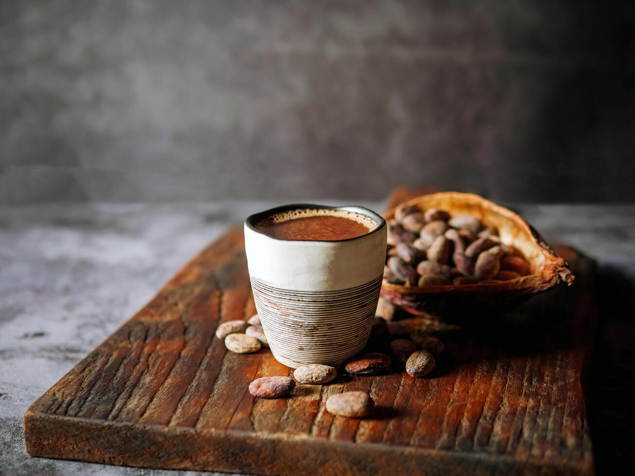 Natural craft cocoa drink on wooden tray, organic healthy chocolate drink with brown cocoa beans and dry cacao pod photo