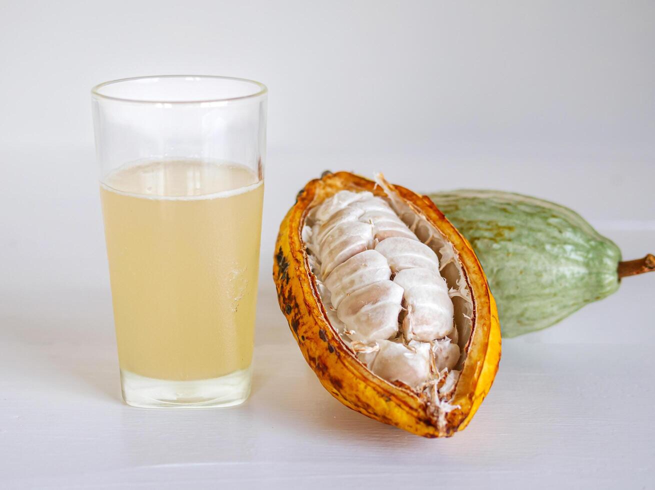 Fresh cacao water in glass and half sliced ripe yellow cacao pod with white cocoa seed, Cacao juice in glass on white wooden background photo