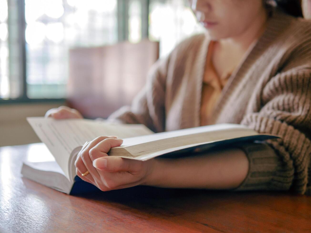 Learning, education Hand of asian woman sitting reading fiction book on wooden table in the morning,relax and enjoy books. photo