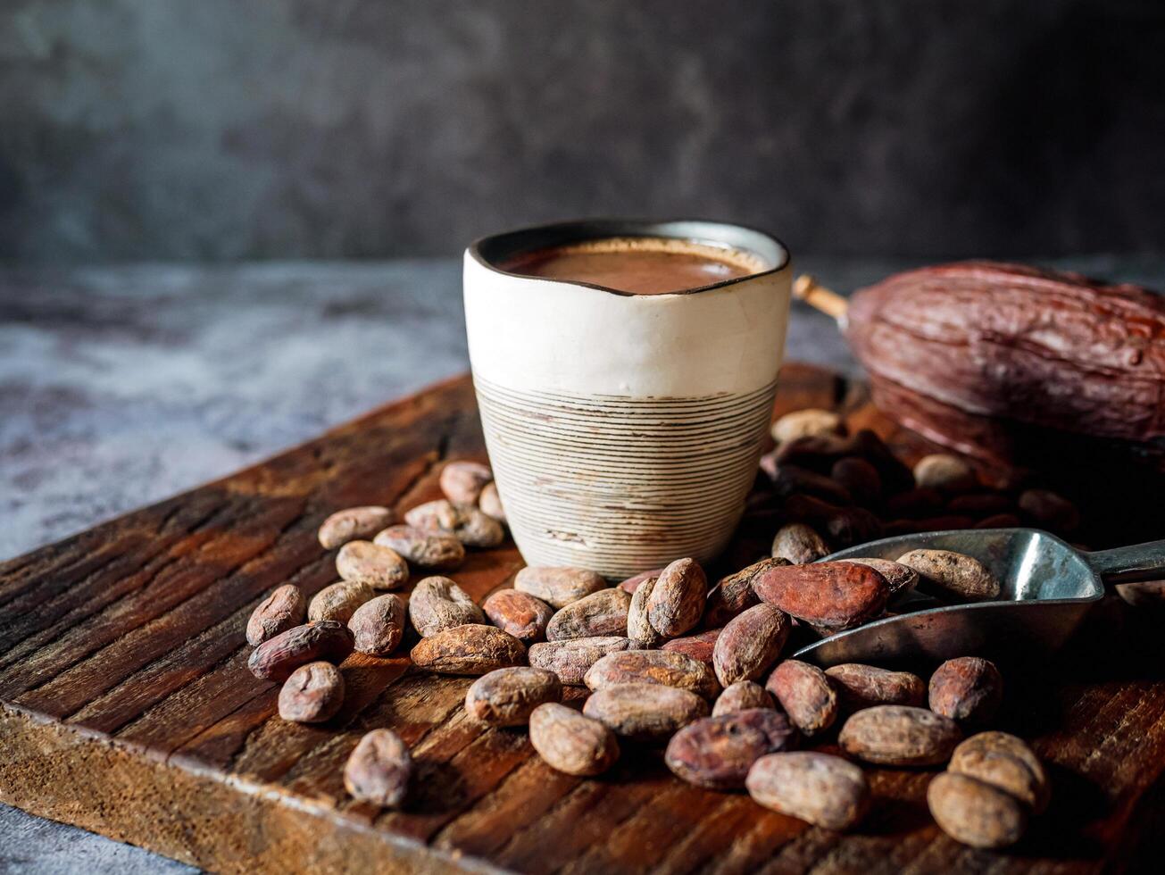 Natural craft cocoa drink on wooden tray, organic healthy chocolate drink with brown cocoa beans and dry cacao pod photo
