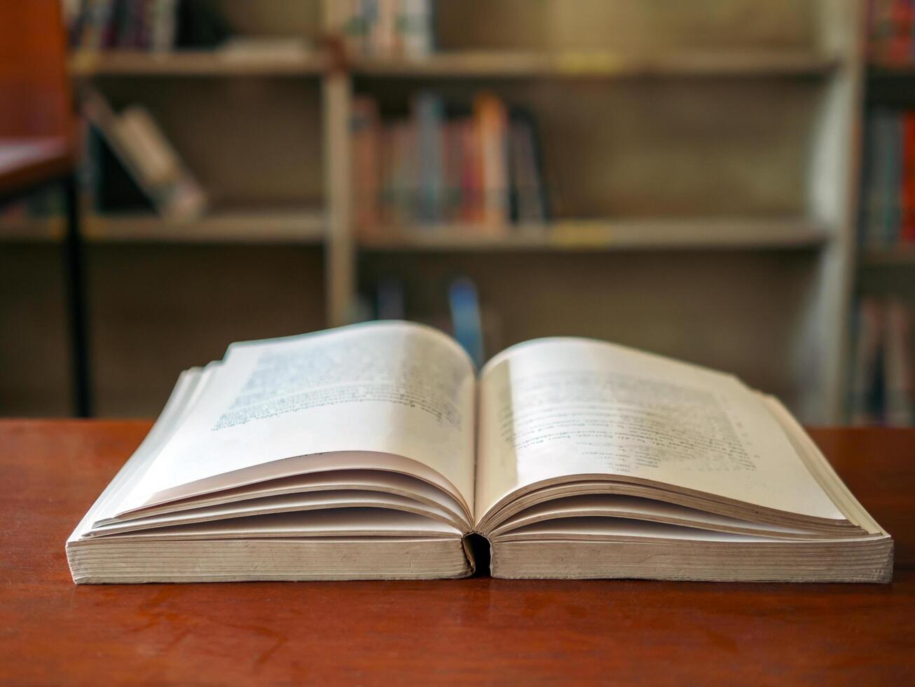 An open book or textbook vintage style on wooden table in the library and the bookshelves background.Education learning concept photo