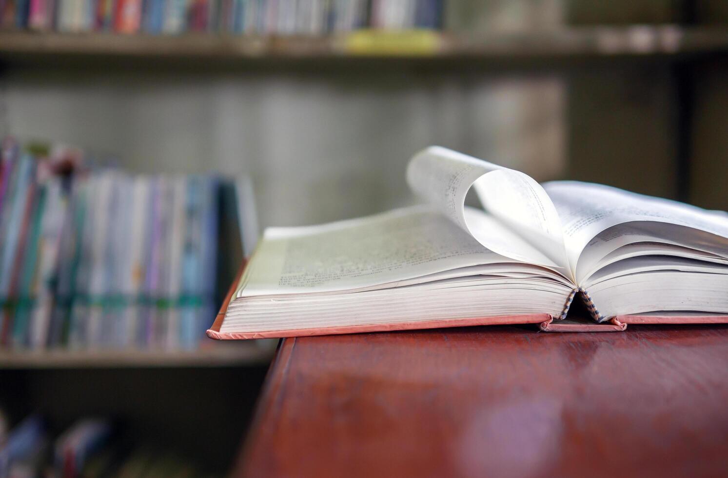 An open book or textbook vintage style on wooden table in the library and the bookshelves background.Education learning concept photo