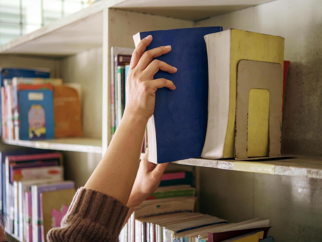 The hands of a woman taking out a book from the bookshelf photo