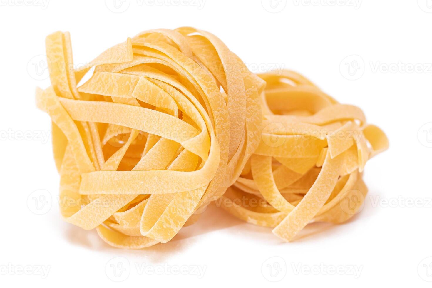 Two Classic Italian Raw Egg Fettuccine - Isolated on White Background. Dry Twisted Uncooked Pasta. Italian Culture and Cuisine. Raw Golden Macaroni Pattern - Isolation photo