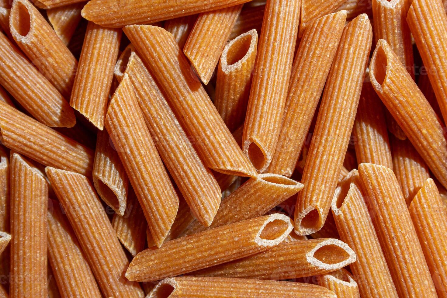 Uncooked Whole Grain Penne Rigate Pasta. A Culinary Canvas of Whole Wheat Macaroni, Creating a Lively and Textured Background for Gourmet Cooking. Whole Grain Dry Pasta. Whole Wheat Raw Macaroni photo