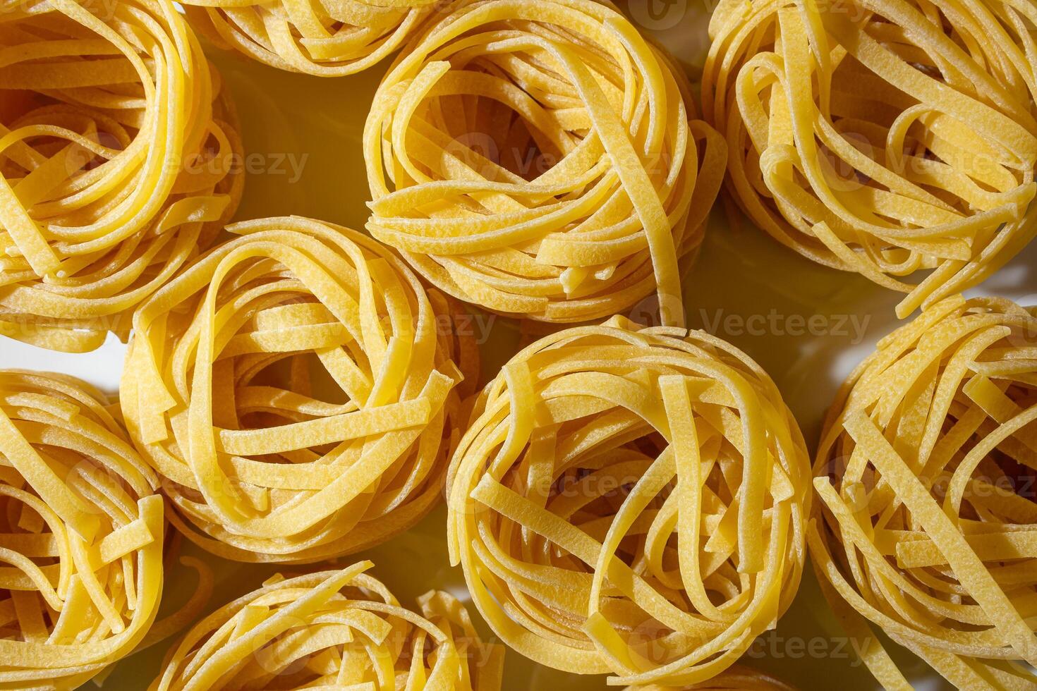 Uncooked Egg-Based Fettuccine Pasta. A Culinary Canvas of Ribbon-Shaped Macaroni, Creating a Lively and Textured Background for Gourmet Cooking. Dry Pasta. Raw Macaroni - Top View, Flat Lay photo