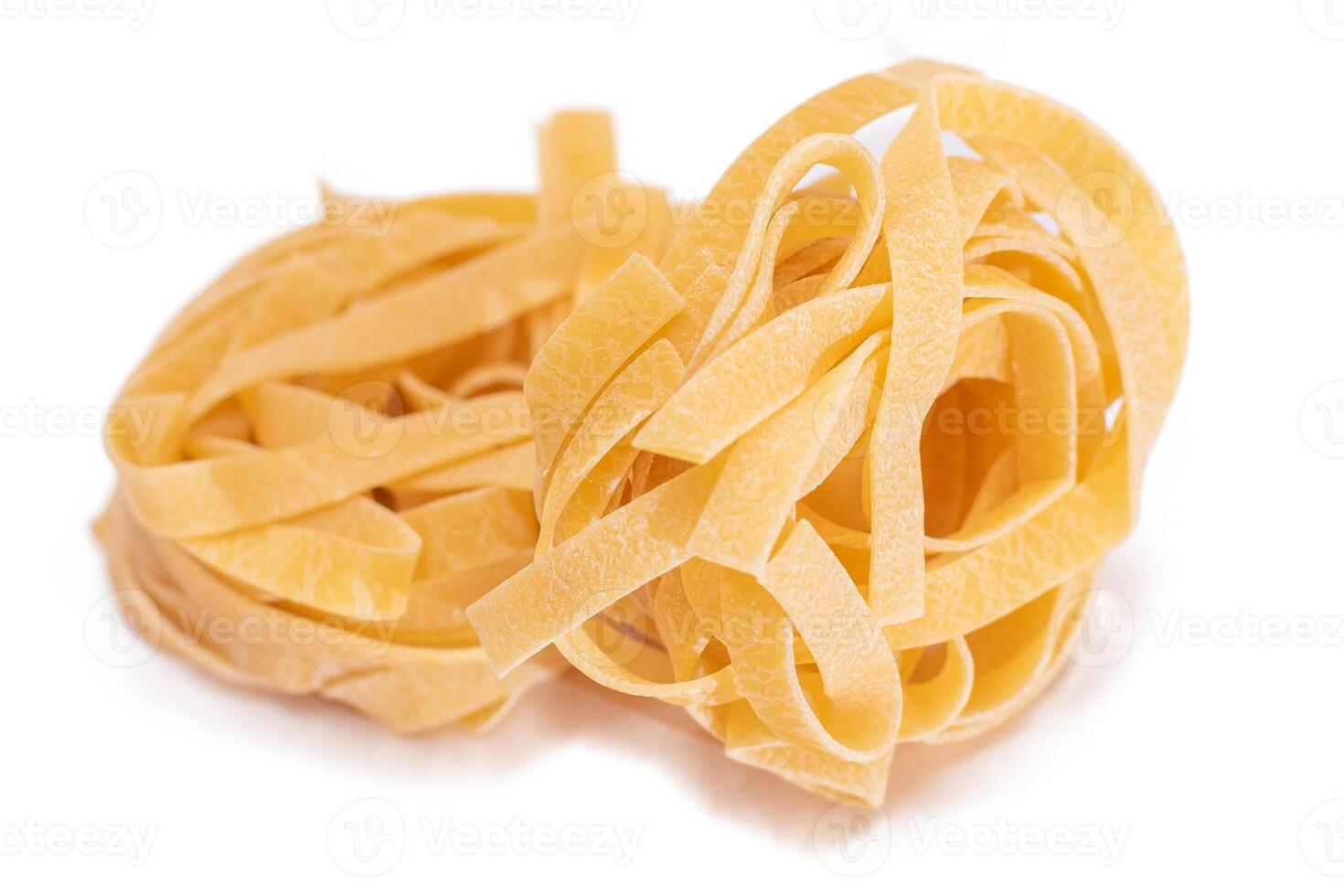 Two Classic Italian Raw Egg Fettuccine - Isolated on White Background. Dry Twisted Uncooked Pasta. Italian Culture and Cuisine. Raw Golden Macaroni Pattern - Isolation photo