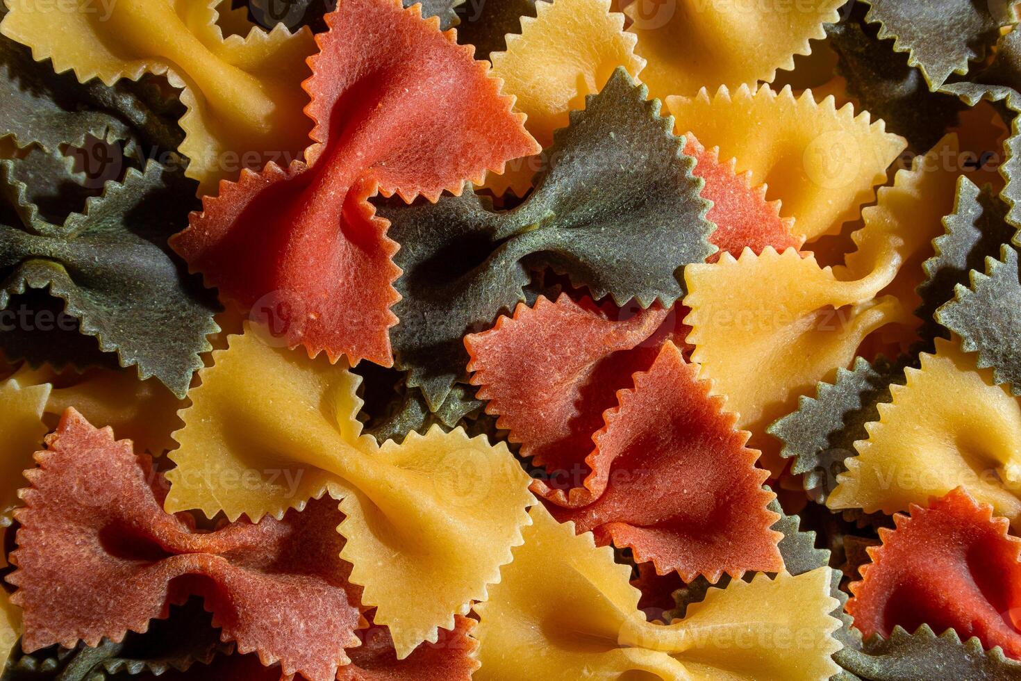 Uncooked Vibrant Colored Farfalle Pasta. A Culinary Canvas of Multicolored Bow-Tie Macaroni, Creating a Lively and Textured Background for Gourmet Cooking Enthusiasts. Colored Dry Pasta. Raw Macaroni photo