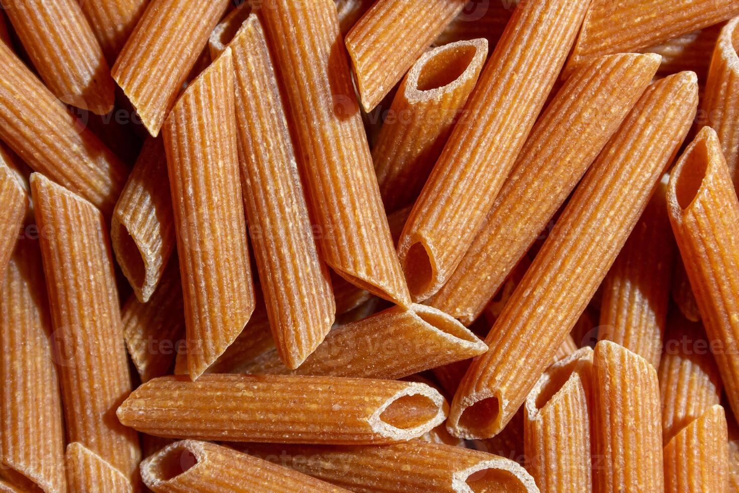 Uncooked Whole Grain Penne Rigate Pasta. A Culinary Canvas of Whole Wheat Macaroni, Creating a Lively and Textured Background for Gourmet Cooking. Whole Grain Dry Pasta. Whole Wheat Raw Macaroni photo