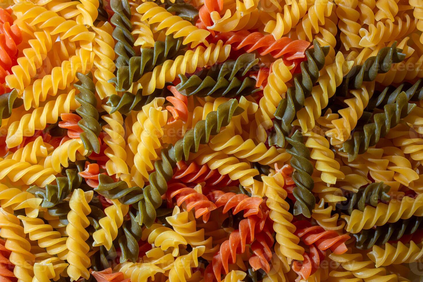 Uncooked Vibrant Colored Fusilli Pasta. A Mesmerizing Culinary Canvas of Multicolored Spirals, Creating a Lively and Textured Background for Gourmet Cooking. Colored Dry Pasta. Raw Macaroni photo