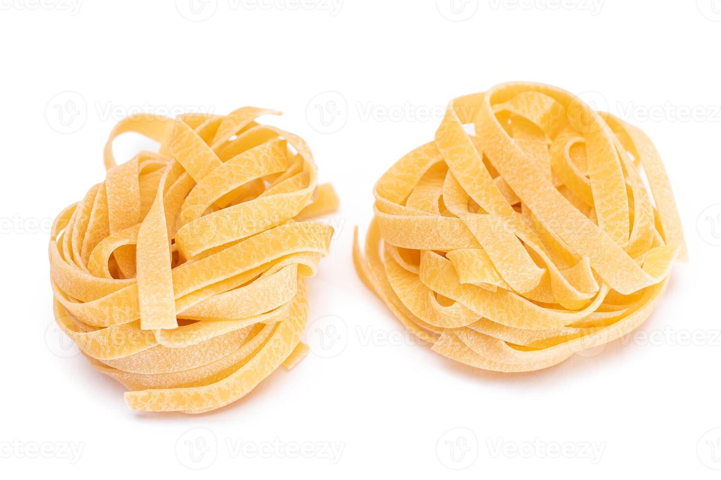 Two Classic Italian Raw Egg Fettuccine - Isolated on White Background. Dry Twisted Uncooked Pasta. Italian Culture and Cuisine. Raw Golden Macaroni Pattern - Isolation photo