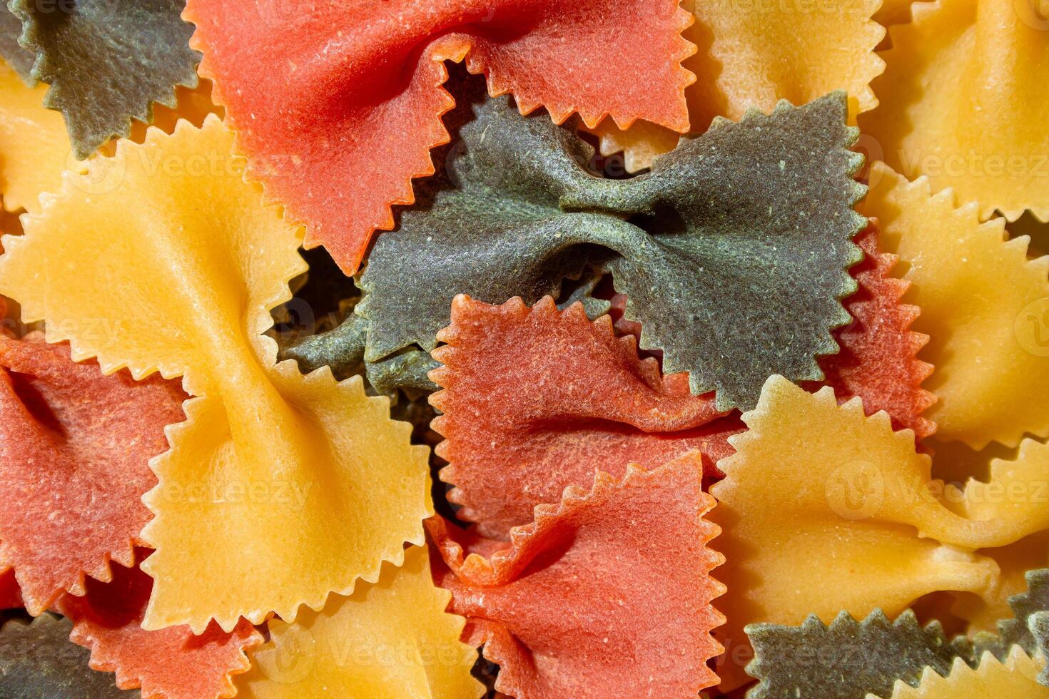Uncooked Vibrant Colored Farfalle Pasta. A Culinary Canvas of Multicolored Bow-Tie Macaroni, Creating a Lively and Textured Background for Gourmet Cooking Enthusiasts. Colored Dry Pasta. Raw Macaroni photo