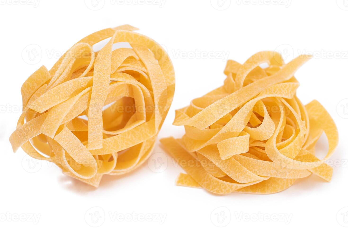 Two Classic Italian Raw Egg Fettuccine - Isolated on White Background. Dry Twisted Uncooked Pasta. Italian Culture and Cuisine. Raw Golden Macaroni Pattern - Isolation photo