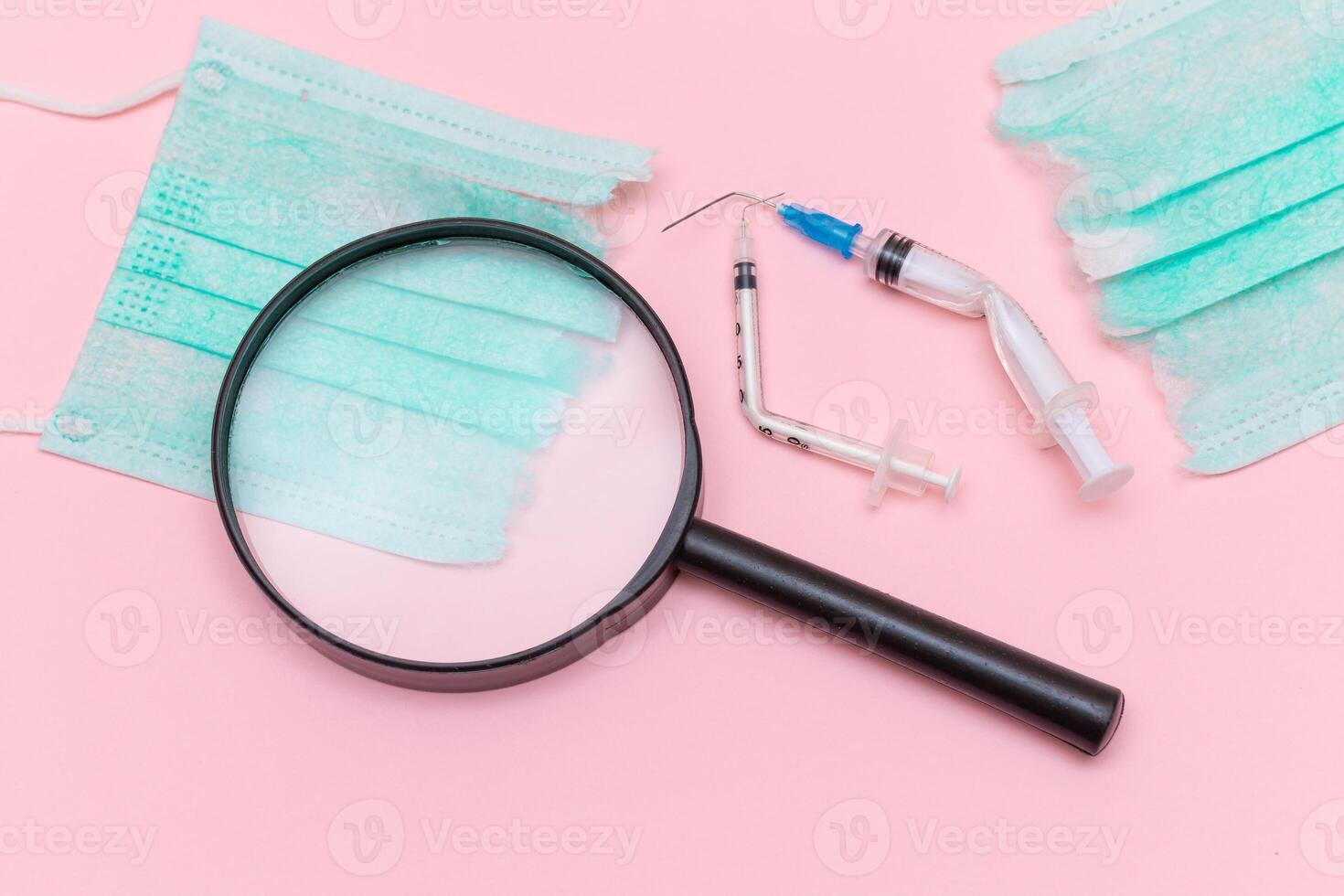 Anti Vaccine Movement and Anti Mask Concept - Broken Medical Syringe and Green Torn Medical Face Mask with Magnifying Glass on the Pink Background. Pandemic and Lockdown End - Top View, Flat Lay photo