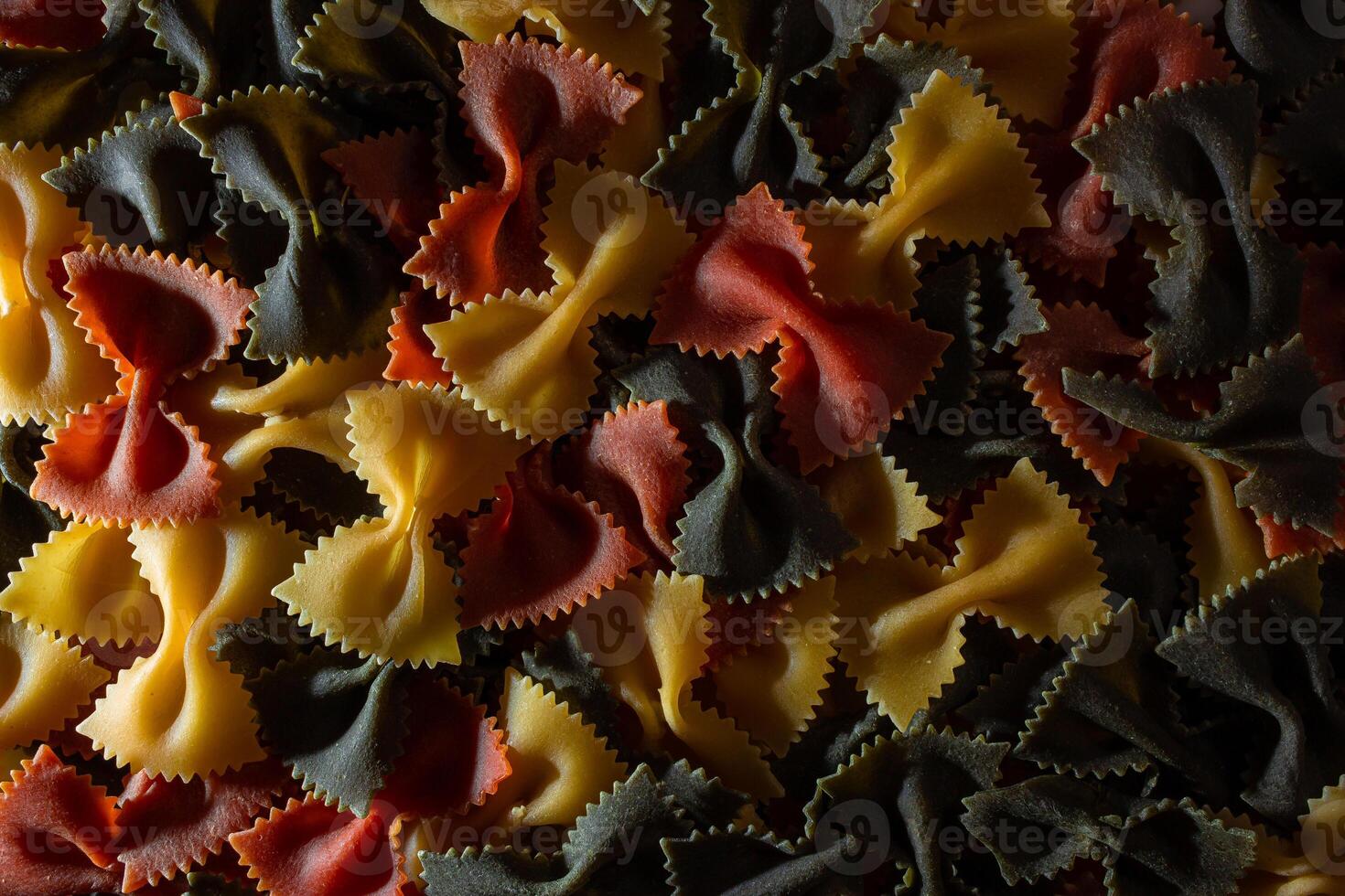 Uncooked Vibrant Colored Farfalle Pasta. A Culinary Canvas of Multicolored Bow-Tie Macaroni, Creating a Lively and Textured Background for Gourmet Cooking Enthusiasts. Colored Dry Pasta. Raw Macaroni photo