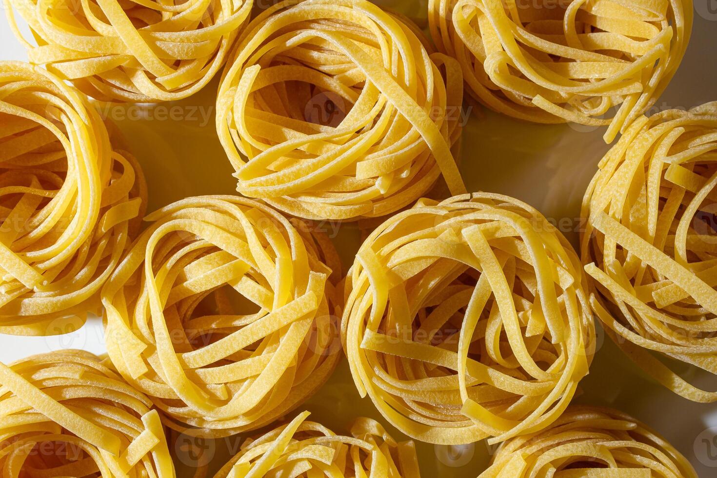 Uncooked Egg-Based Fettuccine Pasta. A Culinary Canvas of Ribbon-Shaped Macaroni, Creating a Lively and Textured Background for Gourmet Cooking. Dry Pasta. Raw Macaroni - Top View, Flat Lay photo