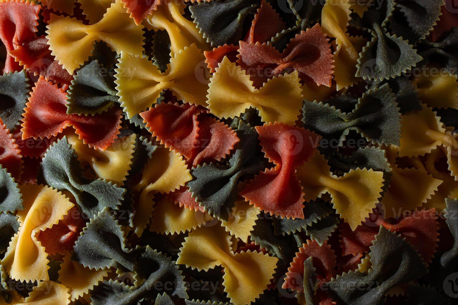 Uncooked Vibrant Colored Farfalle Pasta. A Culinary Canvas of Multicolored Bow-Tie Macaroni, Creating a Lively and Textured Background for Gourmet Cooking Enthusiasts. Colored Dry Pasta. Raw Macaroni photo