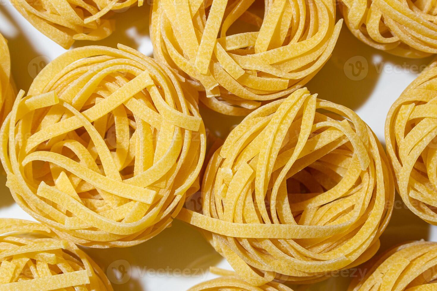 Uncooked Egg-Based Fettuccine Pasta. A Culinary Canvas of Ribbon-Shaped Macaroni, Creating a Lively and Textured Background for Gourmet Cooking. Dry Pasta. Raw Macaroni - Top View, Flat Lay photo