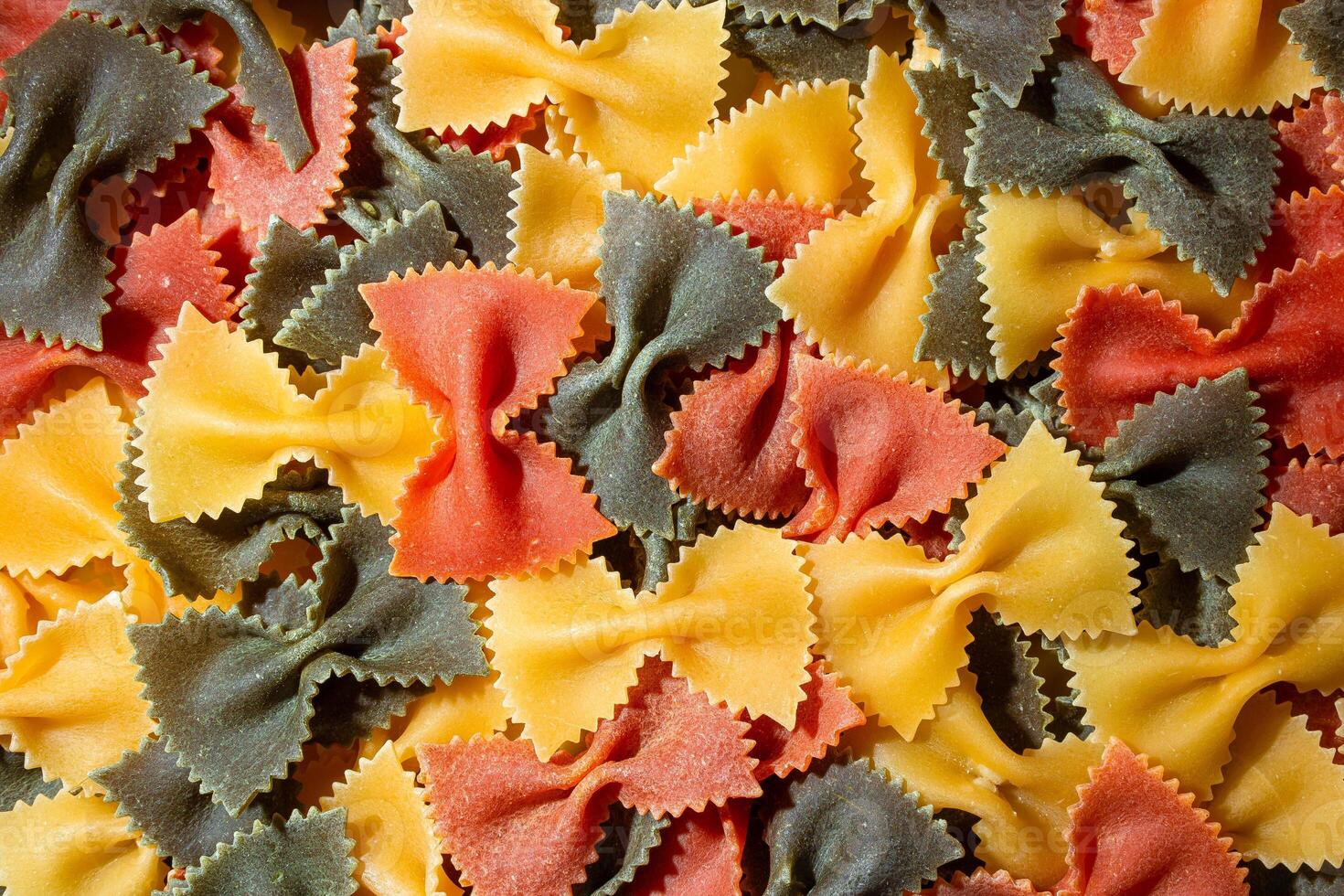 Uncooked Vibrant Colored Farfalle Pasta. A Culinary Canvas of Multicolored Bow-Tie Macaroni, Creating a Lively and Textured Background for Gourmet Cooking Enthusiasts. Colored Dry Pasta. Raw Macaroni photo