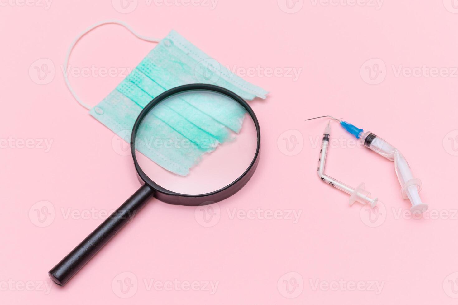 Anti Vaccine Movement and Anti Mask Concept - Broken Medical Syringe and Green Torn Medical Face Mask with Magnifying Glass on the Pink Background. Pandemic and Lockdown End - Top View, Flat Lay photo