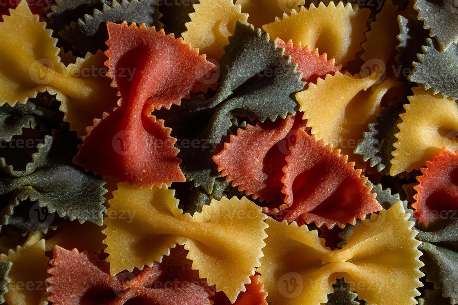 Uncooked Vibrant Colored Farfalle Pasta. A Culinary Canvas of Multicolored Bow-Tie Macaroni, Creating a Lively and Textured Background for Gourmet Cooking Enthusiasts. Colored Dry Pasta. Raw Macaroni photo